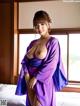 A woman in a purple kimono posing on a bed.