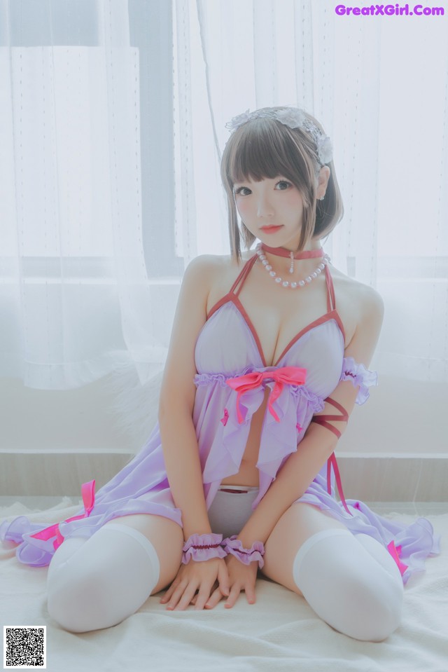 A woman in a purple and pink lingerie sitting on a bed.
